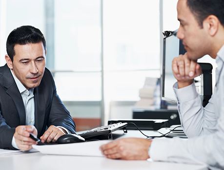 Man in business suit reviews report with another person while sitting at a conference table