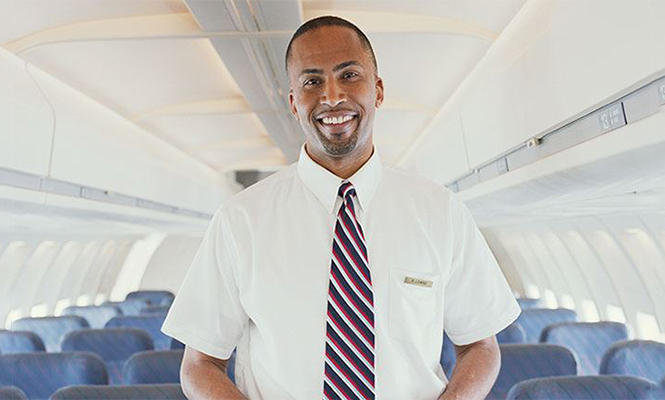 A male flight attendant standing in an airplane aisle smile at the camera