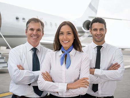 Trio of flight attendants smile at camera with plane in the background