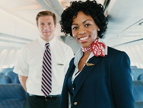 Female flight attendant stands in airplane aisle and smiles at camera