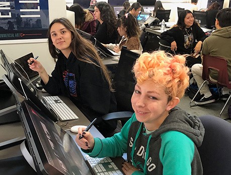 Two women drawing on computers in a classroom