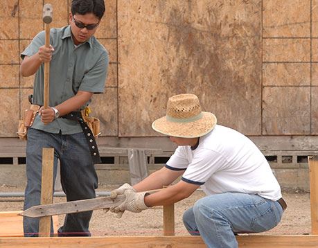 Two men hammer together the frame of a house