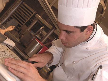 Culinary worker finely chops herbs on a cutting board