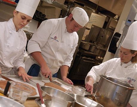 Three culinology professionals spread batter on a baking sheet