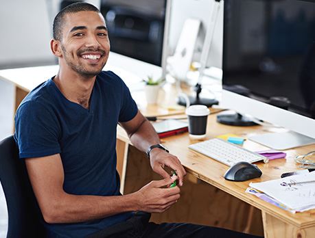 Male sitting at a computer work station smiles at camera