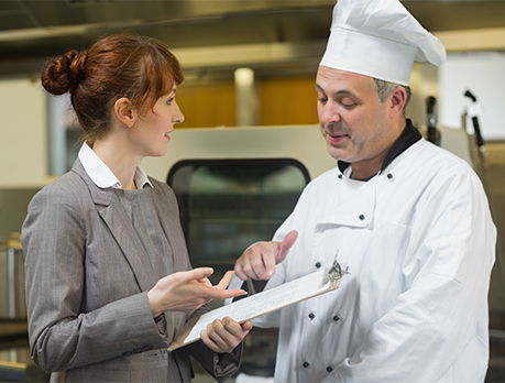 Female restaurant manager consults with male cook in a commercial kitchen