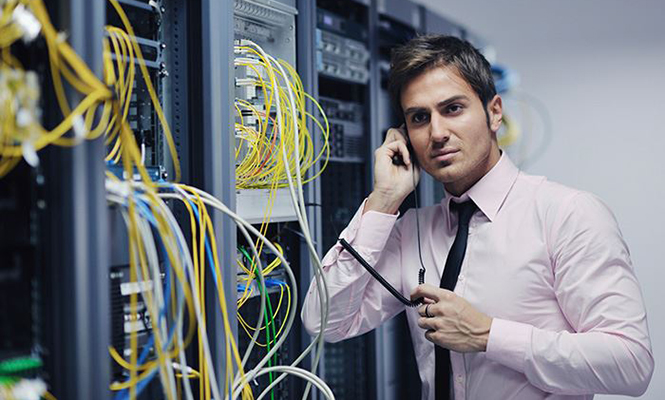 Male network administrator talks on phone next to computer servers