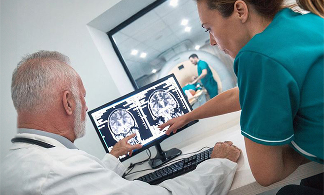 A female neurodiagnostic technician reviews a brain scan on a computer monitor with a physician