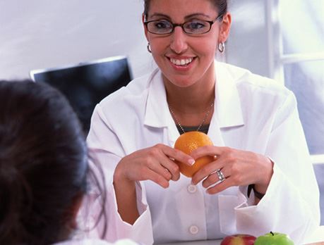 Nutritionist smiles at a patient while holding an orange, with more fruit on the table