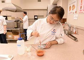 Culinology assistant tests a red sauce with an instrument