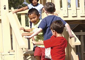 Four preschool students run up stairs together on a playground