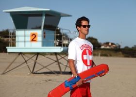 A male lifeguard holding a flotation device on a beach looks out into the water