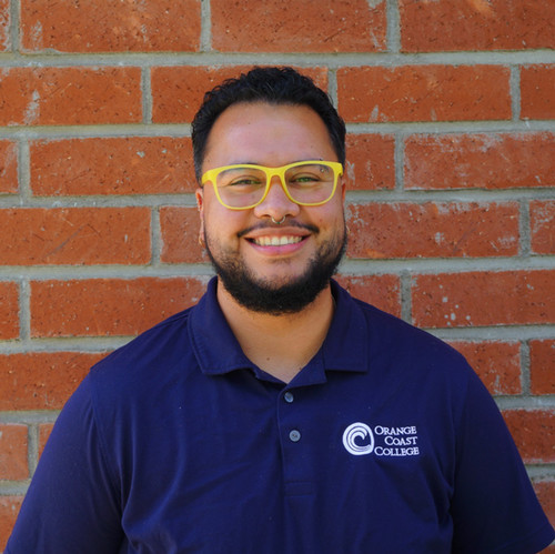 LGBTQIA+ project specialist Caleb standing in front of bamboo and smiling.